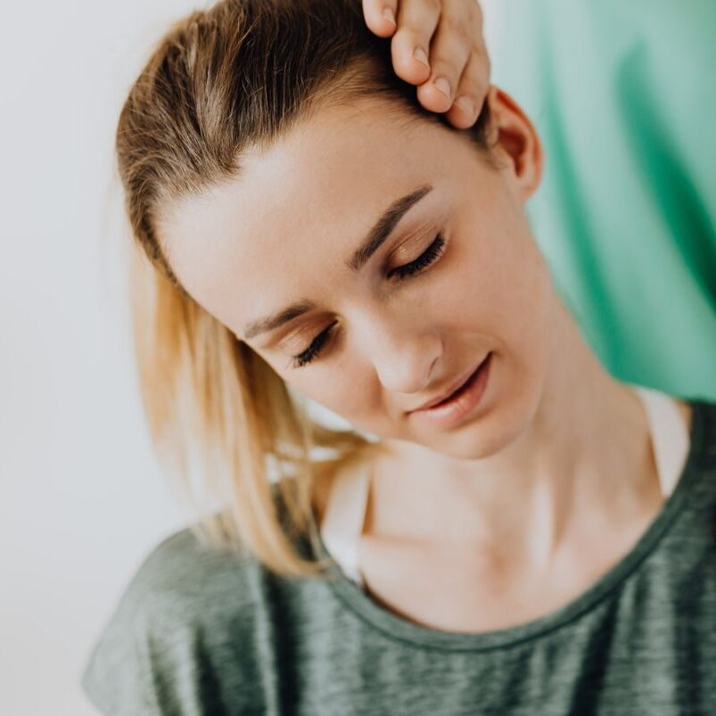 Crop professional male massage therapist in green medical uniform doing therapeutic neck massage on content female patient wearing casual clothes